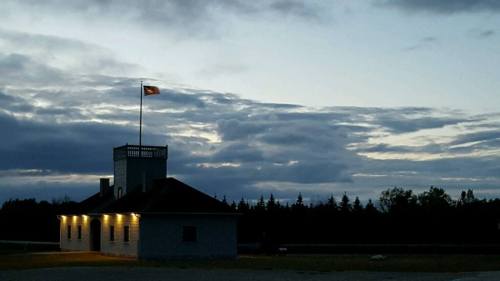 A small building with a flag on top, illuminated by lights, against a cloudy twilight sky.