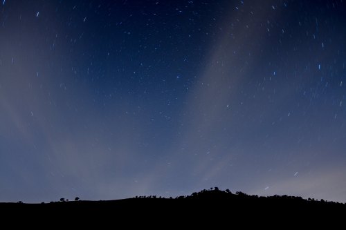 A night sky filled with stars, with a dark silhouette of a mountain range at the bottom.