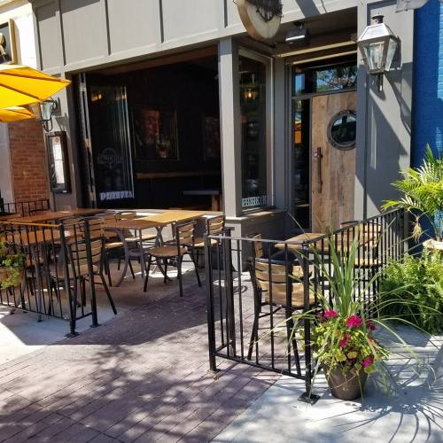 Outdoor seating area of a restaurant with tables, chairs, and potted plants, featuring a welcoming entrance.