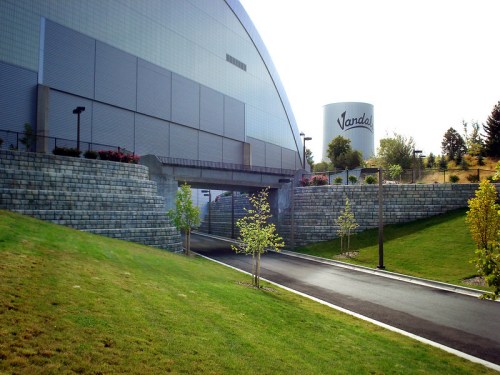 A pathway leads to a large, modern building with a water tower labeled "Vandal" in the background, surrounded by greenery.