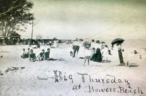 Black and white photo of people enjoying a beach day at Bowers Beach, with umbrellas and vintage clothing.