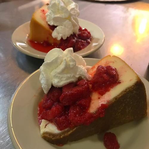 Two slices of cheesecake topped with raspberry sauce and whipped cream, served on white plates.
