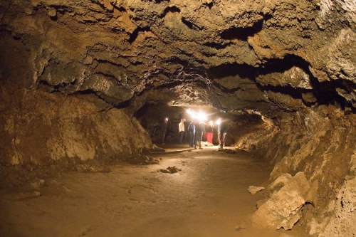 A dimly lit cave with rocky walls and a sandy floor, featuring a group of people walking in the distance.