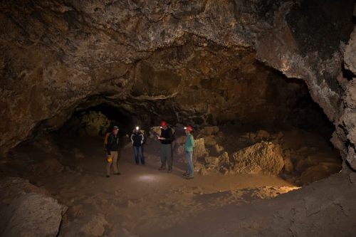 A group of five people with headlamps exploring a dark cave, surrounded by rocky walls and uneven terrain.