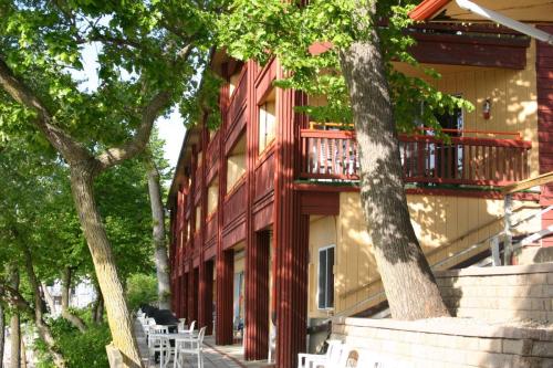 A wooden building with balconies, surrounded by trees and outdoor seating, near a waterfront.