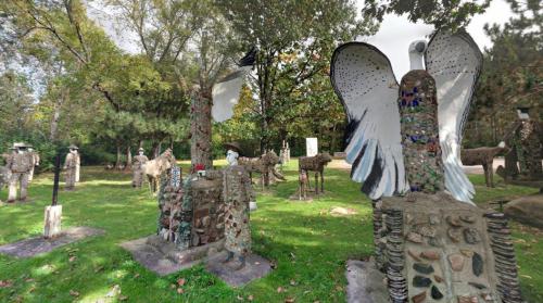 A whimsical outdoor art installation featuring various sculptures, including birds and figures, set in a green park.