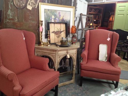 Two vintage red checkered armchairs flanking a small table with a framed painting and decorative items in a rustic setting.