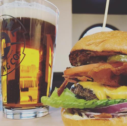 A close-up of a juicy cheeseburger with bacon, lettuce, and tomato, alongside a glass of amber beer.