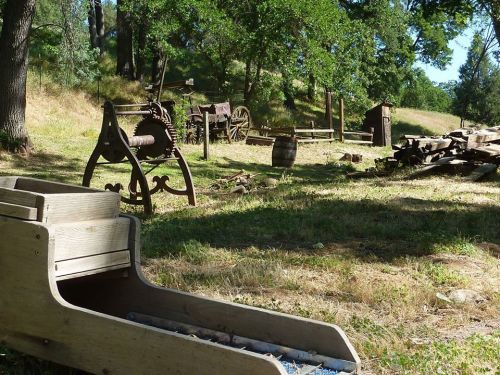 A rustic outdoor scene featuring vintage farming equipment, wooden structures, and a grassy landscape.