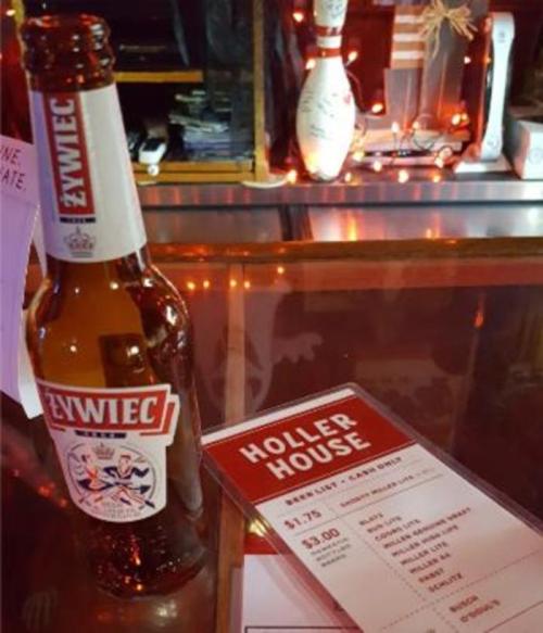 A bottle of Żywiec beer next to a menu at Holler House, with festive lights in the background.
