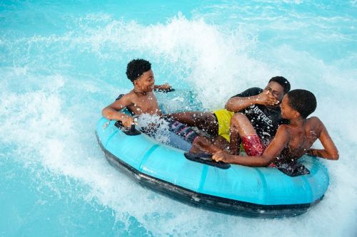 Three boys enjoying a fun ride on a blue inflatable tube in a splash-filled pool.