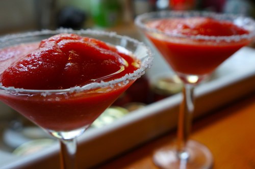 Two frozen strawberry cocktails in salt-rimmed glasses, garnished with a vibrant red slush on top.