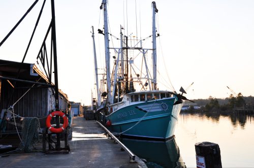 Fishing boat docked at a pier during sunrise, with fishing gear and calm water in the background.