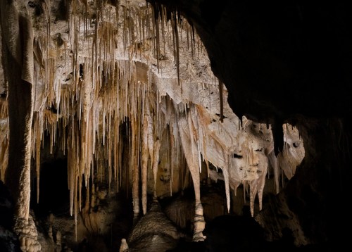 Stalactites and stalagmites hang from the ceiling of a dark cave, creating a dramatic underground landscape.