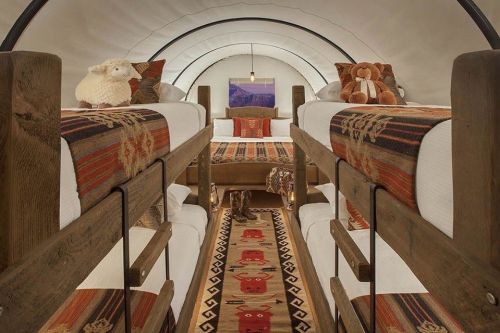 Cozy interior of a tent-style room with bunk beds, decorative rugs, and plush toys on the beds. Warm, inviting atmosphere.