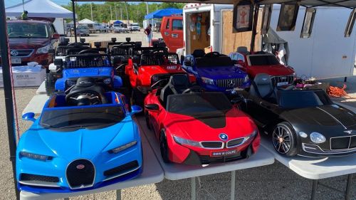 A row of toy cars in various colors and styles displayed on a table at an outdoor market.