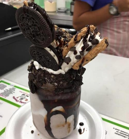 A tall dessert jar filled with chocolate ice cream, topped with whipped cream, Oreos, chocolate syrup, and cookie pieces.
