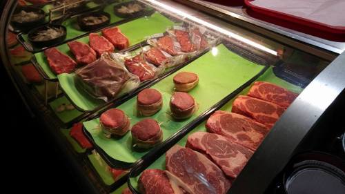 A display case filled with various cuts of raw meat, including steaks and ground meat, on green trays.