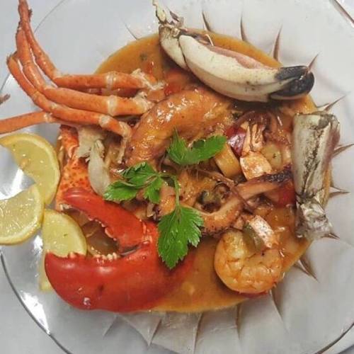 A vibrant seafood dish featuring shrimp, crab, and lobster, garnished with lemon and fresh herbs in a clear bowl.