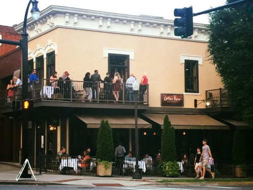 A bustling restaurant with outdoor seating, people dining, and a lively atmosphere on a warm evening.