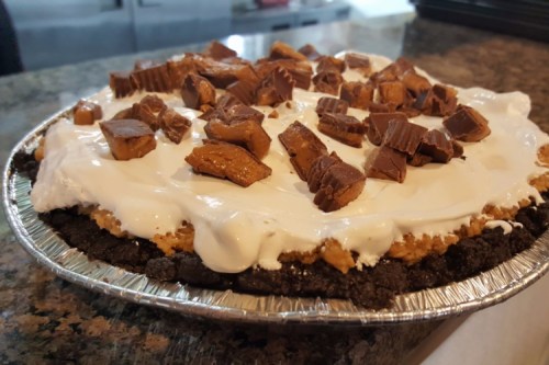 A pie with a chocolate crust, topped with whipped cream and chunks of caramel candy.