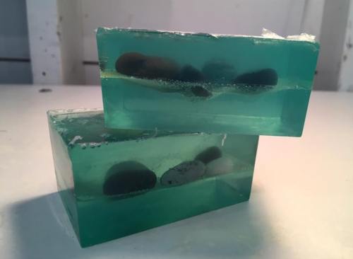 Two translucent green soap bars with embedded dark stones, stacked on a white surface.