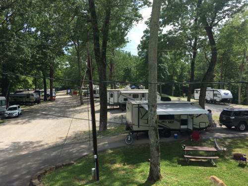 A view of a campground with several RVs parked along a tree-lined road, surrounded by greenery.