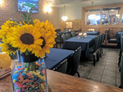 A cozy restaurant interior with tables set for dining and a vase of sunflowers on the counter.