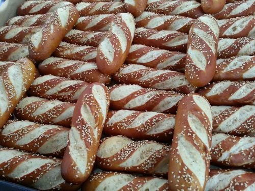 A close-up of freshly baked pretzel rolls, golden brown with sesame seeds, arranged in a neat pile.