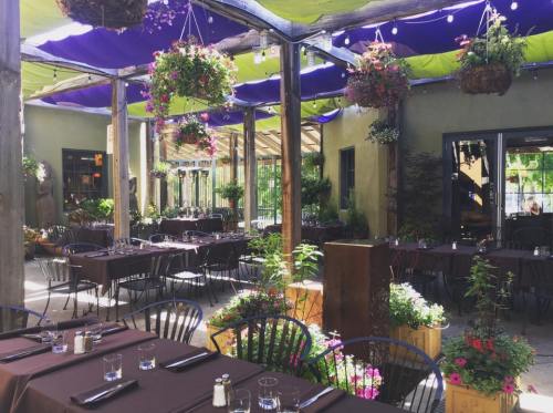 A vibrant outdoor dining area with tables, hanging plants, and colorful canopies, creating a lively atmosphere.