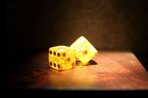 Two translucent yellow dice with black dots, illuminated against a dark background, resting on a wooden surface.