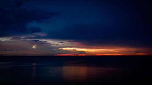A serene sunset over the ocean, with dark clouds and vibrant colors reflecting on the water's surface.