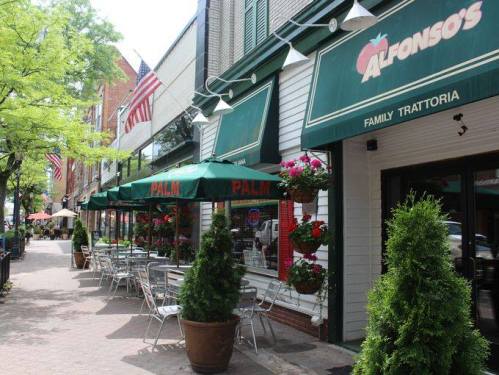 A charming street view of Alfonso's Family Trattoria, featuring outdoor seating and vibrant flower arrangements.