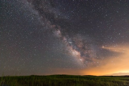 A stunning view of the Milky Way galaxy illuminated against a dark night sky, with a grassy landscape below.