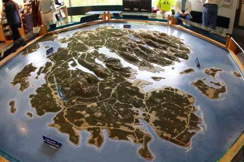 A detailed topographical model of an island, showcasing hills, forests, and water features, viewed from above.