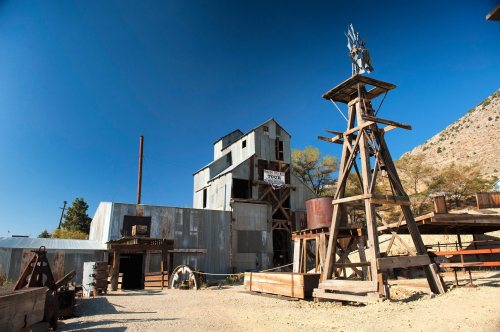 Historic mining structure with a windmill, surrounded by rustic wooden buildings and a clear blue sky.