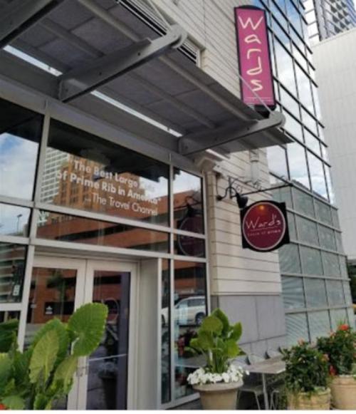 Exterior of Ward's restaurant featuring a sign and large windows, with plants in front and a city backdrop.