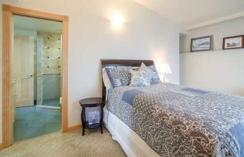 Cozy bedroom with a patterned bedspread, bedside lamp, and an open door leading to a bathroom.