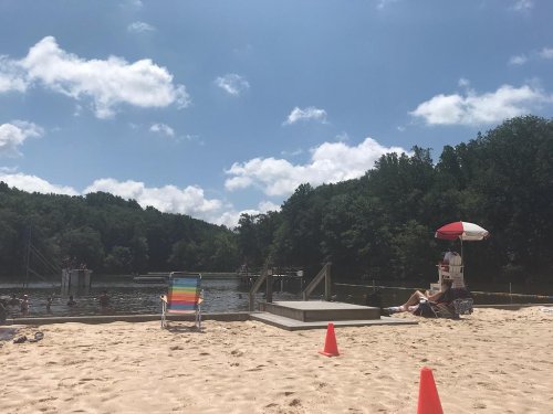 A sandy beach with colorful chairs, a lifeguard stand, and people enjoying the water under a sunny sky.