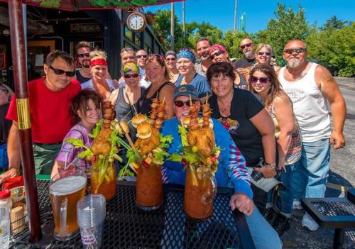 A lively group of people poses together at an outdoor gathering, featuring large drinks with garnishes in the foreground.