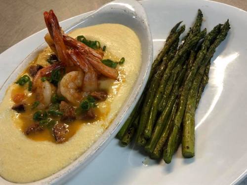 A dish featuring shrimp on creamy grits, garnished with green onions, alongside grilled asparagus.