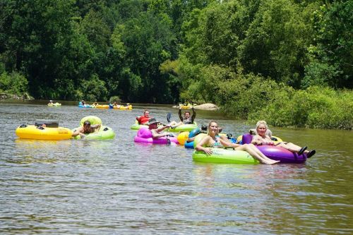 A group of people floating on colorful inner tubes in a river, surrounded by lush greenery and a sunny sky.