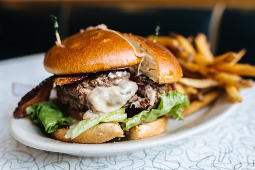 A juicy burger with melted cheese, lettuce, and bacon, served with a side of crispy fries on a white plate.