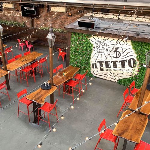 Outdoor dining area with wooden tables, red chairs, string lights, and a green wall featuring the "Il Letto" sign.