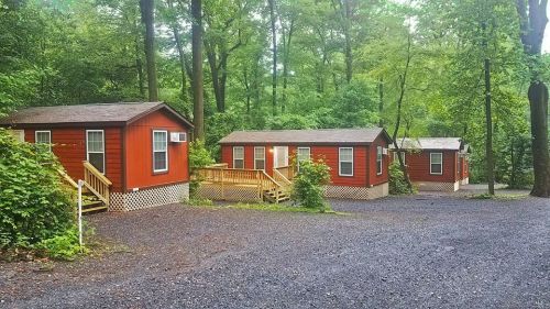 Three red cabins nestled in a lush green forest, surrounded by trees and a gravel pathway.