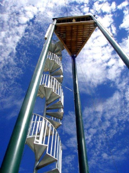 A tall spiral staircase leading up to a platform against a blue sky with scattered clouds.