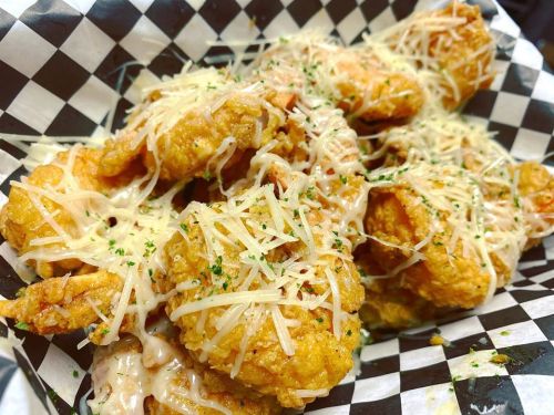 Crispy fried chicken pieces topped with melted cheese and herbs, served in a black and white checkered basket.