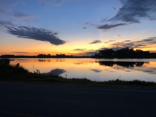 A serene sunset over a calm lake, with colorful clouds reflecting on the water's surface and a silhouette of trees.