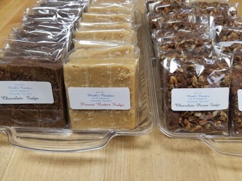 A clear container holds three types of fudge: chocolate, peanut butter, and chocolate pecan, each labeled.