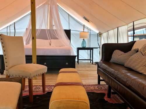 Interior of a glamping tent featuring a bed, seating area, and decorative elements like a lamp and rug.